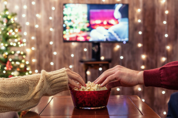 Christmas eve. Couple watching tv and eating popcorn. Home cinema. Cropped, close up Holiday Streaming and Gaming Without Buffering